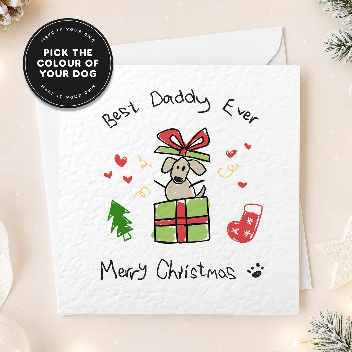 A white Christmas greeting card with a hand-drawn illustration of a dog sitting on a green gift box with a red bow, surrounded by small red hearts, a green tree, a red stocking, and the text 'Best Daddy Ever' and 'Merry Christmas'. A black circular badge in the top left says 'Pick the colour of your dog' and 'Make it your own'.